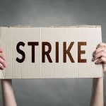Two hands holding a cardboard sign saying STRIKE