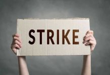 Two hands holding a cardboard sign saying STRIKE