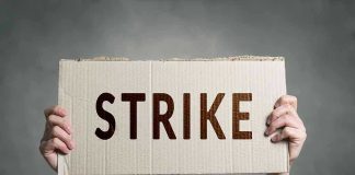 Two hands holding a cardboard sign saying STRIKE