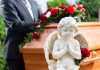 A stone angel statue with roses in front of a wooden casket at a funeral service