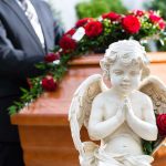 A stone angel statue with roses in front of a wooden casket at a funeral service