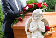 A stone angel statue with roses in front of a wooden casket at a funeral service