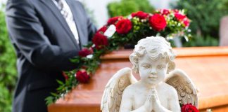 A stone angel statue with roses in front of a wooden casket at a funeral service