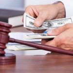 A person counting cash in a courtroom setting with a gavel in the foreground
