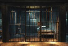 Empty prison cell with metal bars and bed.
