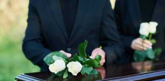 People placing white roses on a casket.