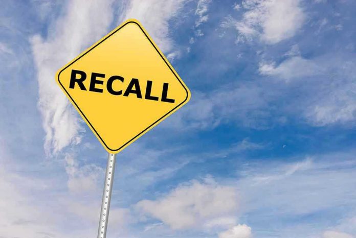 529192612 Yellow recall sign against blue, cloudy sky.
