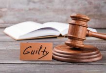 A wooden gavel next to a card that reads 'Guilty' and an open book