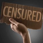 A hand holding a cardboard sign that reads 'CENSORED'