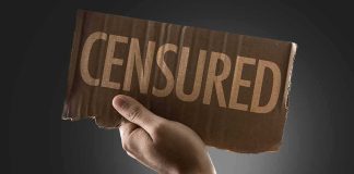 A hand holding a cardboard sign that reads 'CENSORED'