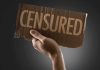 A hand holding a cardboard sign that reads CENSORED