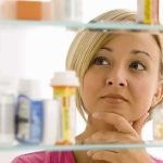 A woman thoughtfully looking at a medicine cabinet filled with various medications