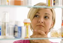 A woman thoughtfully looking at a medicine cabinet filled with various medications