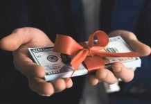 SHOCKING $130 Million Military Gift—Who Paid? Hands holding stack of hundred-dollar bills with ribbon.