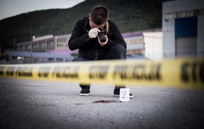 702059647 Crime scene photographer behind police tape with evidence marker.