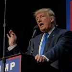 Trump Banner Sparks SHOCKING Gunfire Showdown Person speaking into microphone at a podium.