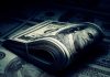 A rolled stack of hundred dollar bills on a background of more banknotes