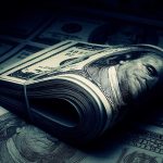 A rolled stack of hundred dollar bills on a background of more banknotes