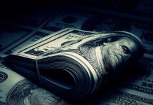 A rolled stack of hundred dollar bills on a background of more banknotes