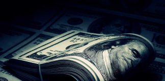 A rolled stack of hundred dollar bills on a background of more banknotes