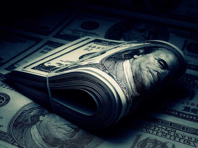 A rolled stack of hundred dollar bills on a background of more banknotes