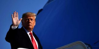 A political figure waving while standing on the steps of airforce one