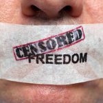 Close up of a persons mouth covered with tape that reads CENSORED FREEDOM
