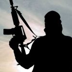 Silhouette of a person holding a rifle against a cloudy sky