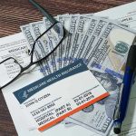 Medicare card glasses pen money on wooden table