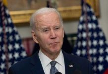 Biden Aides’ Shocking Cover-Up Allegations Explode Man in suit speaking, flanked by American flags.