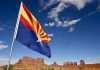 Grand Canyon Horror — Man Falls to Death Arizona state flag waving in front of Monument Valley under a blue sky