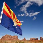 Grand Canyon Horror — Man Falls to Death Arizona state flag waving in front of Monument Valley under a blue sky