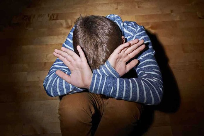 A child sitting on the floor with their hands covering their face, expressing distress