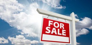 A red For Sale sign against a blue sky with clouds