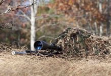 A sniper rifle partially covered in camouflage netting in a grassy area