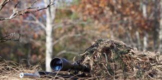 A sniper rifle partially covered in camouflage netting in a grassy area