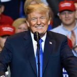 Trump’s Bold Doctrine: Global Shake-Up Ahead Man in suit speaking at rally with red hats.