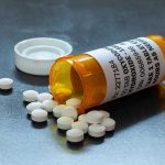 Husband DRUGS Wife — Films It Open pill bottle with white tablets spilled out.