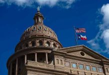 Building dome with US and Texas flags, blue sky.