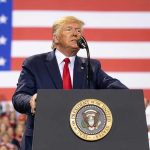 Trade War Escalation—Trump Targets USMCA Man speaks at podium with U.S. flag background.