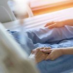 Hospital patient holding visitors hand reassuringly.