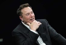 Musk’s God Bombshell Shocks Silicon Valley Man in suit smiling, resting chin on hand.