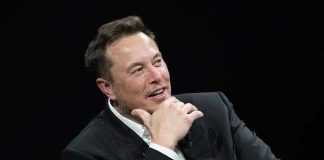 Musk’s God Bombshell Shocks Silicon Valley Man in suit smiling, resting chin on hand.
