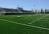 Empty football field with bleachers in background.