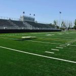 Football Scandal Explodes: Coach Arrested Empty football field with bleachers in background.