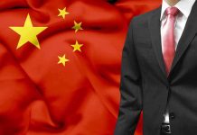 A man in a suit stands in front of the Chinese flag