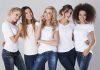 Five women in white t-shirts and jeans smiling together