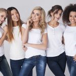 Five women in white t-shirts and jeans smiling together