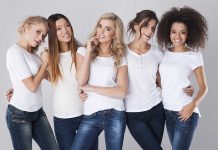 Five women in white t-shirts and jeans smiling together