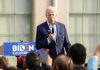 Man speaking at an outdoor event with Biden sign.